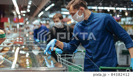 customer in protective gloves looking at the products in the refrigerator 84382412