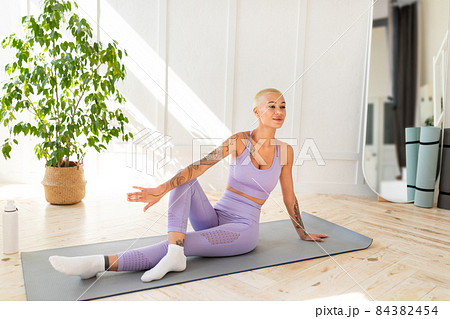 Peaceful woman sitting in yoga pose and smiling, exercising on training mat in living room interior, free space 84382454