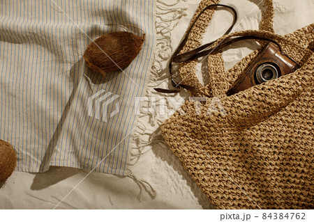 Striped linen beach towel with fringes, woven bag, vintage camera and coconut on sandy beach with shadows from palm tree. Relaxation and tropical summer holidays concept 84384762
