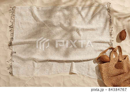 Striped linen beach towel with fringes and two coconuts on sandy beach with shadows from palm tree. Relaxation and tropical summer holidays concept Striped linen beach towel with fringes and two coconuts on sandy beach with shadows from palm tree. Relaxation and tropical summer holidays concept 84384767