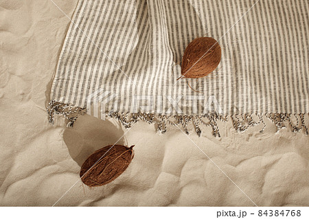 Striped linen beach towel with fringes and two coconuts on sandy beach with shadows from palm tree. Relaxation and tropical summer holidays concept Striped linen beach towel with fringes and two coconuts on sandy beach with shadows from palm tree. Relaxation and tropical summer holidays concept 84384768