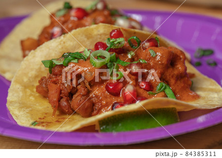Traditional Mexican tacos with meat and vegetables in purple paper plates served for takeaway on wood table. Mexican food background. 84385311