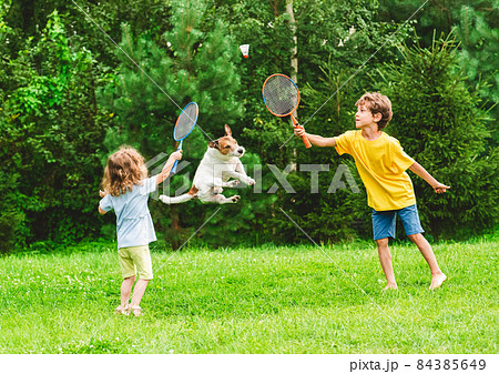 Kids having fun playing badminton and dog jumping up to catch and steal shuttlecock Kids having fun playing badminton and dog jumping up to catch and steal shuttlecock 84385649
