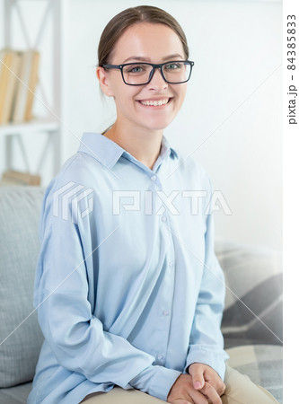 Intelligent woman portrait. Success motivation. Psychotherapy wellbeing. Confident cheerful smiling smart female mentor in eyeglasses on couch at light home interior. Intelligent woman portrait. Success motivation. Psychotherapy wellbeing. Confident cheerful smiling smart female mentor in eyeglasses on couch at light home interior. 84385833