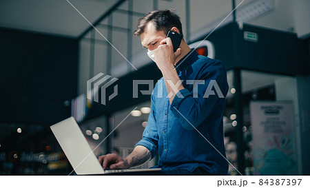 young man in a protective mask is choosing a contact in his smartphone 84387397