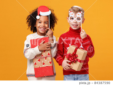 Happy multiracial children in warm knitted sweaters holding Christmas party glasses and gift boxes 84387590