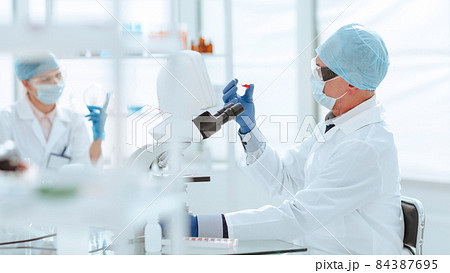 scientist with an ampoule of a new vaccine sitting at a laboratory table 84387695