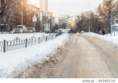 Empty city road covered by dirt melted snow sludge after heavy snowfall against street building cityscape warm sunset sun light. Cold season bad weather extreme driving conditions. Slippery driveway Empty city road covered by dirt melted snow sludge after heavy snowfall against street building cityscape warm sunset sun light. Cold season bad weather extreme driving conditions. Slippery driveway 84389216