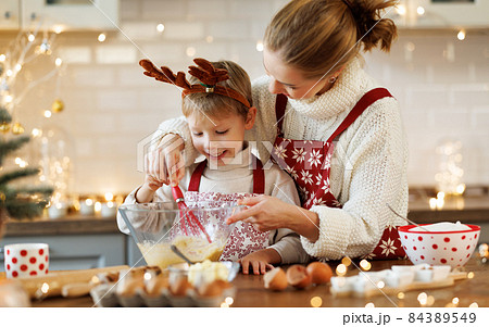 Cute little son boy helping mother to make dough for Christmas cookies in cozy kitchen at home 84389549