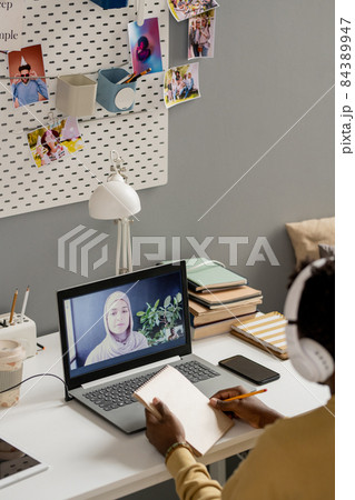 African guy with pencil and notepad sitting by desk in front of laptop 84389947