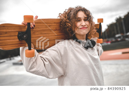 Girl with skateboard on shoulders standing in park 84390925