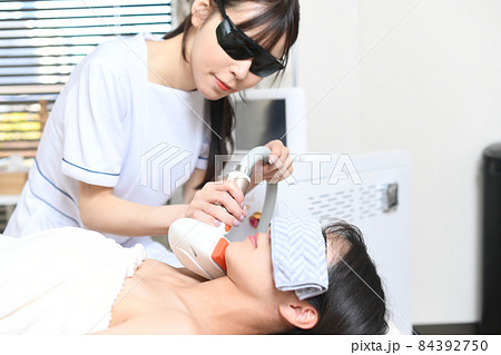 サロンの機械で脱毛の施術をするスタッフと女性のお客 84392750
