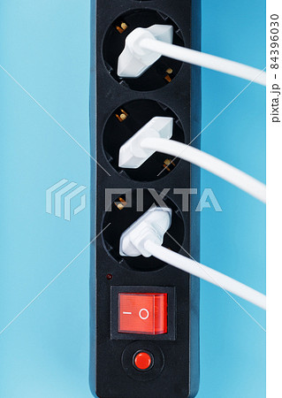 A black mains filter with electrical outlets inserted into it with white plugs of electrical appliances on a blue background A black mains filter with electrical outlets inserted into it with white plugs of electrical appliances on a blue background 84396030