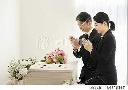 棺の前で手を合わせる喪服姿の男女 84396517