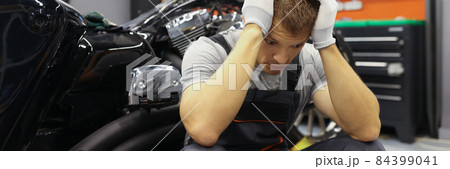 Master locksmith with headache sits near motorcycle at service station Master locksmith with headache sits near motorcycle at service station 84399041
