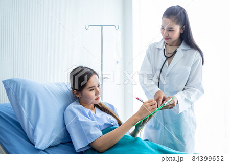 Asian young female patient Signature for consent form on bed to female doctor therapeutic advising with positive emotions in the room hospital background. 84399652