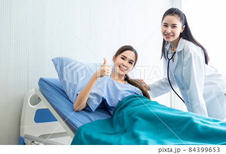Asian young female patient on bed showing thumbs up with smiley face very good symptom to asian young female nurse doctor in hospital background. 84399653