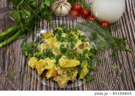 Fried potatoes with mushrooms decoration of herbs in a glass plate on a wooden background. Fried potatoes with mushrooms decoration of herbs in a glass plate on a wooden background. 84399804