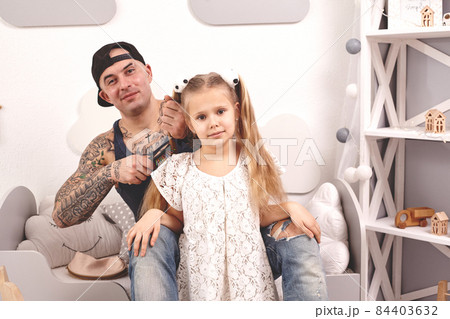 Funny time Tattoed father in a cap and his child are playing at home. Dad is doing his daughter's hair in her bedroom. Family holiday and togetherness Funny time Tattoed father in a cap and his child are playing at home. Dad is doing his daughter's hair in her bedroom. Family holiday and togetherness 84403632