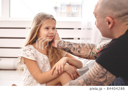 Adorable daughter wearing a white dress whith her loving father in a modern kid's room whith a wooden furniture. Happy family. 84404286