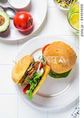 Vegan burger with avocado, tomato and nut sauce, white tile background, top view. Plant-based diet concept. 84404606