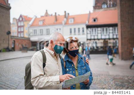 Senior couple tourists with face masks using map outdoors in town street Senior couple tourists with face masks using map outdoors in town street 84405141
