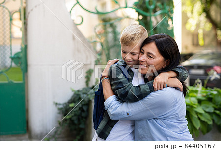 Happy schoolboy hugging his grandmother waiting for him after school outdoors in street. Happy schoolboy hugging his grandmother waiting for him after school outdoors in street. 84405167
