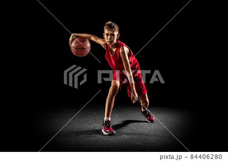 Full-length portrait of teen boy, professional backetball player in motion, training isolated over black background 84406280