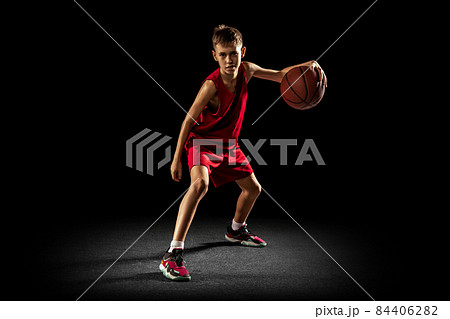 Full-length portrait of teen boy, professional backetball player in motion, training isolated over black background. Dribbling action 84406282