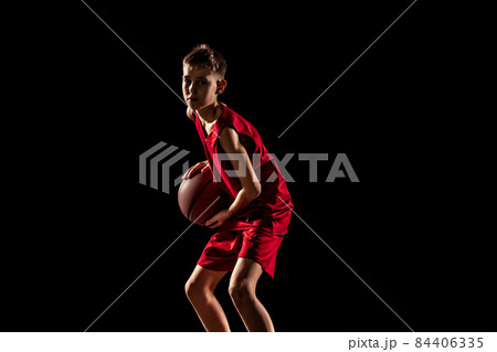 Cropped portrait of boy, basketball player in special uniform training isolated over black background 84406335