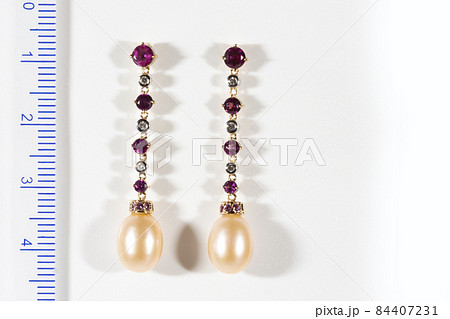 Long gold earrings with diamonds, rubies and pearls, on a white background next to the ruler Long gold earrings with diamonds, rubies and pearls, on a white background next to the ruler 84407231