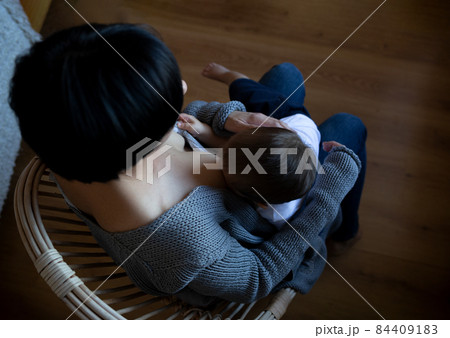 young woman breastfeeding her little son while sitting in a cozy armchair young woman breastfeeding her little son while sitting in a cozy armchair 84409183