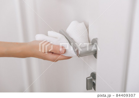 Cleaning black door handles with an antiseptic wet wipe. Sanitize surfaces prevention in hospital and public spaces against corona virus. Woman hand using towel for cleaning. 84409307
