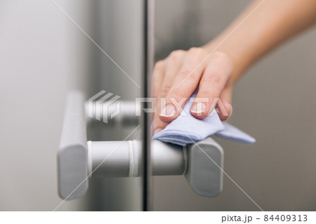 Cleaning glass door handles with an antiseptic wet wipe. Sanitize surfaces prevention in hospital and public spaces against corona virus. Woman hand using towel for cleaning home room door link. Cleaning glass door handles with an antiseptic wet wipe. Sanitize surfaces prevention in hospital and public spaces against corona virus. Woman hand using towel for cleaning home room door link. 84409313