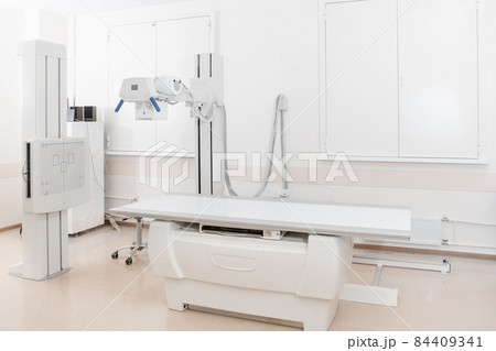 X-ray department in modern hospital. Radiology room with scan machine with empty bed. Technician adjusting an x-ray machine. Scanning chest, heart, lungs in modern clinic office. 84409341