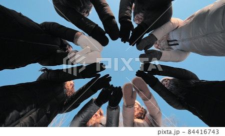 Friends on a winter day join their hands with mittens in a circle. 84416743