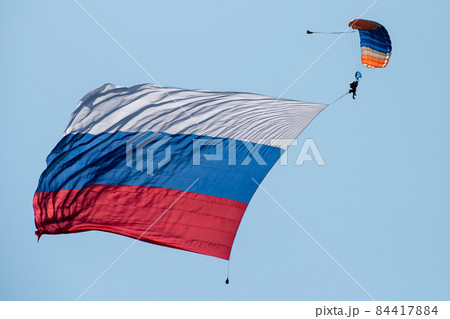Skydiver in the sky with a giant flag of Russia against the blue sky. Skydiver in the sky with a giant flag of Russia against the blue sky. 84417884