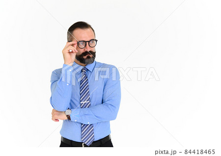Portrait of confident middle-aged businessman in blue shirt and wearing glasses with a beard and mustache standing on white background with copy space 84418465
