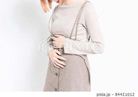 白背景の前に立ってお腹を手で押さえる若い女の子 84421012