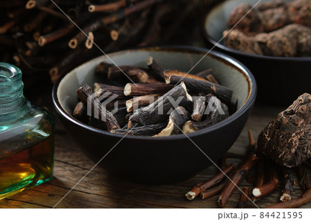 Black bowl of Common comfrey or symphytum officinale roots. Bottle of infusion or tincture. Dried comfrey officinalis roots, knitbone and Bistort, Snakeweed, Snake roots. Alternative herbal medicine. 84421595