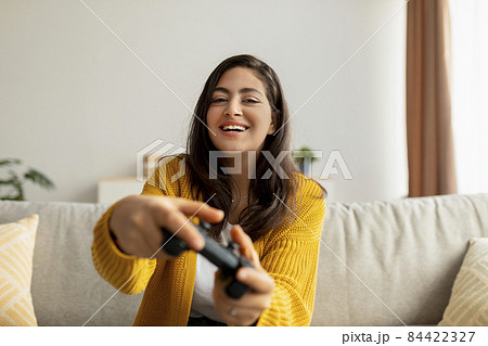 Excited middle eastern lady playing video game with joystick at home, sitting on sofa and smiling, copy space Excited middle eastern lady playing video game with joystick at home, sitting on sofa and smiling, copy space 84422327