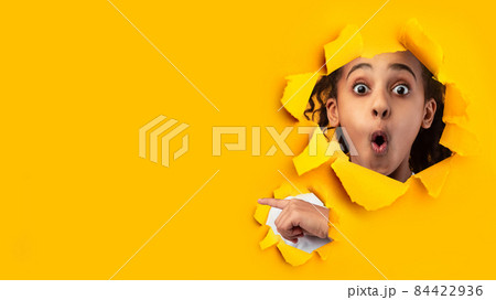 Shocked african american teenage girl with open mouth looks through hole on yellow paper 84422936
