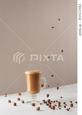 Glass cup with cappuccino and fragrant foam, coconut milk, hazelnuts, planted coffee beans. Coffee concept with vegetarian milk. Cup with cappuccino, latte or coffee with milk. Glass cup with cappuccino and fragrant foam, coconut milk, hazelnuts, planted coffee beans. Coffee concept with vegetarian milk. Cup with cappuccino, latte or coffee with milk. 84423482
