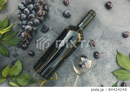 Bottle of red wine, green vine, wineglass and ripe grape on vintage dark stone table background. Top view copy space for text. Wine shop wine bar winery or wine tasting concept Bottle of red wine, green vine, wineglass and ripe grape on vintage dark stone table background. Top view copy space for text. Wine shop wine bar winery or wine tasting concept 84424249
