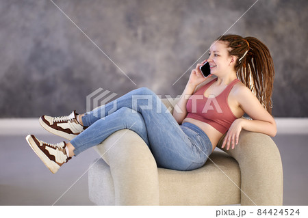 White woman of 28 years old is talking on phone reclining in an armchair. White woman of 28 years old is talking on phone reclining in an armchair. 84424524