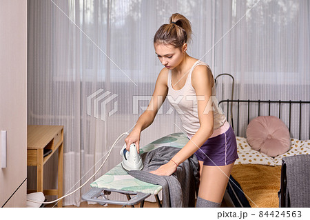 Steam iron for clothes in hands of young European woman who is ironing business suit. 84424563