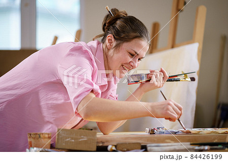 Cute woman paints on canvas in an art workshop. Artist creating picture. Art school or studio. Work with paints, brushes and easel. Hobby and leisure concept. Woman painter at workspace 84426199