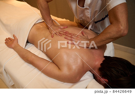 Ayurvedic treatment, professional therapeutic body massage at the wellness spa clinic. A young man relaxes while lying on a massage table during a therapeutic back massage at a luxury spa. Ayurvedic treatment, professional therapeutic body massage at the wellness spa clinic. A young man relaxes while lying on a massage table during a therapeutic back massage at a luxury spa. 84426649