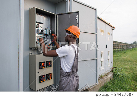 Technician in uniform standing near switchgear at solar farm 84427687