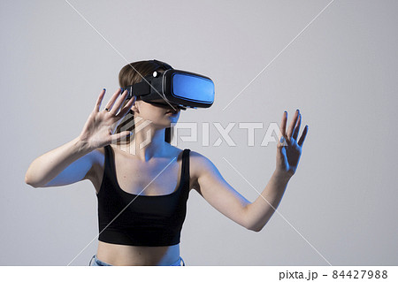 Portrait of young woman playing in VR-glasses in neon light on blue background. Concept modern gadgets and technologies. Future technology concept. Virtual reality gaming. Portrait of young woman playing in VR-glasses in neon light on blue background. Concept modern gadgets and technologies. Future technology concept. Virtual reality gaming. 84427988